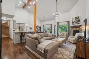 Living area featuring high vaulted ceiling, dark wood-style floors, beamed ceiling, a chandelier, and a stone fireplace