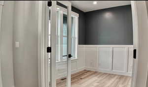 Hallway with light wood-style flooring, wainscoting, a decorative wall, and recessed lighting