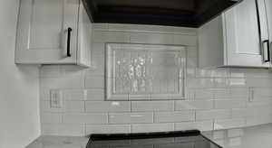 Kitchen view of extractor fan, white cabinetry, light stone counters, and decorative backsplash
