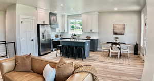 Kitchen with a breakfast bar, stainless steel appliances, light wood-style floors, premium range hood, and a center island