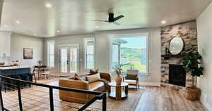 Living room with french doors, light wood-style floors, recessed lighting, a stone fireplace, and ceiling fan