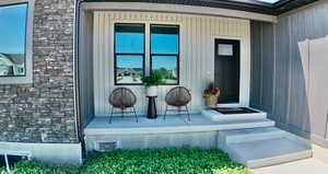 Doorway to property featuring stone siding, covered porch, and board and batten siding