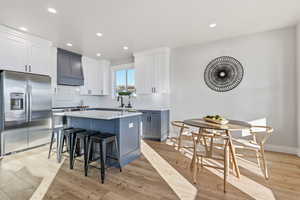 Kitchen featuring stainless steel fridge with ice dispenser, white cabinets, a breakfast bar, recessed lighting, and blue cabinets