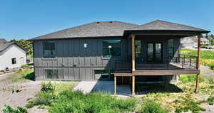 Back of property with board and batten siding, roof with shingles, and a deck