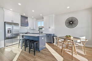 Kitchen featuring stainless steel refrigerator with ice dispenser, white cabinetry, light wood-type flooring, a kitchen breakfast bar, and recessed lighting