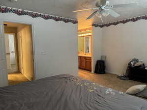Bedroom featuring light colored carpet, a textured ceiling, ensuite bath, and a ceiling fan