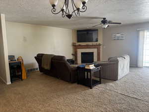 Living room with carpet flooring, a ceiling fan, a chandelier, a tiled fireplace, and a textured ceiling
