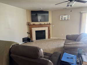Carpeted living room featuring a ceiling fan, a tiled fireplace, and a textured ceiling