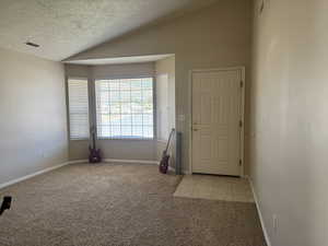 Entrance foyer with light colored carpet, lofted ceiling, a textured ceiling, and light tile patterned floors