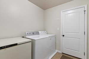 Washroom featuring independent washer and dryer, light tile patterned floors, and a textured ceiling