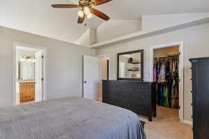 Primary bedroom featuring a spacious closet, light carpet, vaulted ceiling, ensuite bath, and ceiling fan