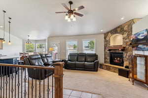 Living area with carpet floors, a stone fireplace, tile patterned floors, a ceiling fan, and a textured ceiling