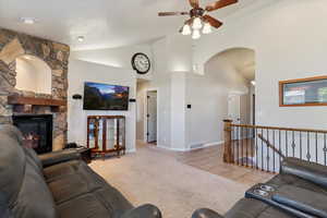 Living area featuring ceiling fan, arched walkways, carpet flooring, a stone fireplace, and high vaulted ceiling