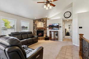 Living room featuring a ceiling fan, vaulted ceiling, light colored carpet, and a fireplace
