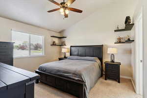 Primary bedroom featuring lofted ceiling, light colored carpet, and a ceiling fan