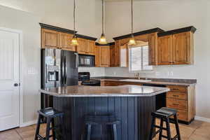Kitchen with light tile patterned floors, black appliances, a breakfast bar area, high vaulted ceiling, and decorative light fixtures