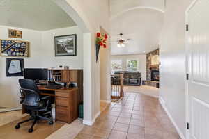 Office space with a fireplace, a ceiling fan, arched walkways, light carpet, and light tile patterned flooring