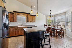 Kitchen featuring refrigerator with ice dispenser, lofted ceiling, light tile patterned floors, a textured ceiling, and dark countertops
