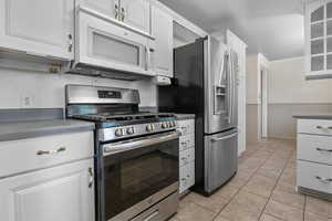 Kitchen featuring stainless steel range with gas cooktop, white microwave, white cabinetry, and light tile patterned flooring