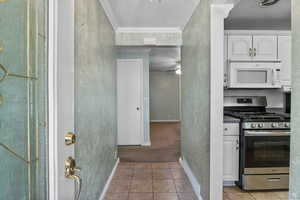 Kitchen featuring gas stove, white microwave, ornamental molding, white cabinetry, and light tile patterned floors