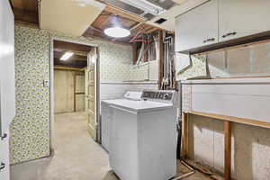 Washroom with washing machine and clothes dryer, cabinet space, and wallpapered walls
