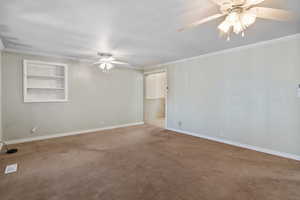 Carpeted spare room featuring ceiling fan, built in features, and ornamental molding