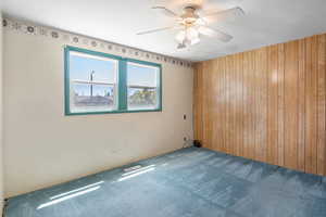 Unfurnished room with wooden walls, carpet flooring, and a ceiling fan