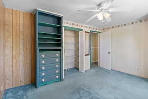 Unfurnished bedroom with two closets, carpet flooring, ceiling fan, and wood walls