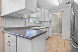 Kitchen featuring dark countertops, freestanding refrigerator, white cabinetry, light tile patterned floors, and white dishwasher