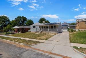 View of front of home featuring covered porch, solar panels, a garage, and concrete driveway