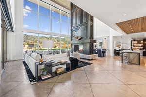 Living room with a towering ceiling, a multi sided fireplace, wooden ceiling, concrete flooring, and recessed lighting