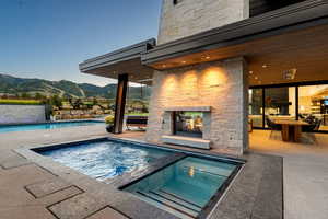 Swimming pool with an outdoor stone fireplace, a mountain view, an in-ground hot tub, and a patio