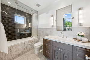 Full bath featuring tile walls, healthy amount of natural light, tile patterned flooring, tiled shower / bath combo, and vanity