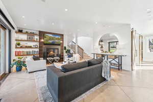 Living area featuring stairs, a glass covered fireplace, recessed lighting, arched walkways, and concrete flooring