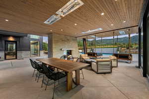Dining room with an outdoor stone fireplace, wooden ceiling, a mountain view, floor to ceiling windows, and recessed lighting