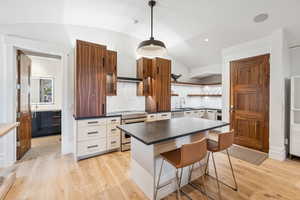 Kitchen featuring appliances with stainless steel finishes, dark countertops, vaulted ceiling, open shelves, and light wood-style flooring