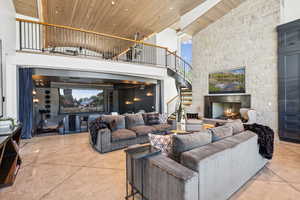 Living room featuring wooden ceiling, a fireplace, stairs, a high ceiling, and finished concrete floors