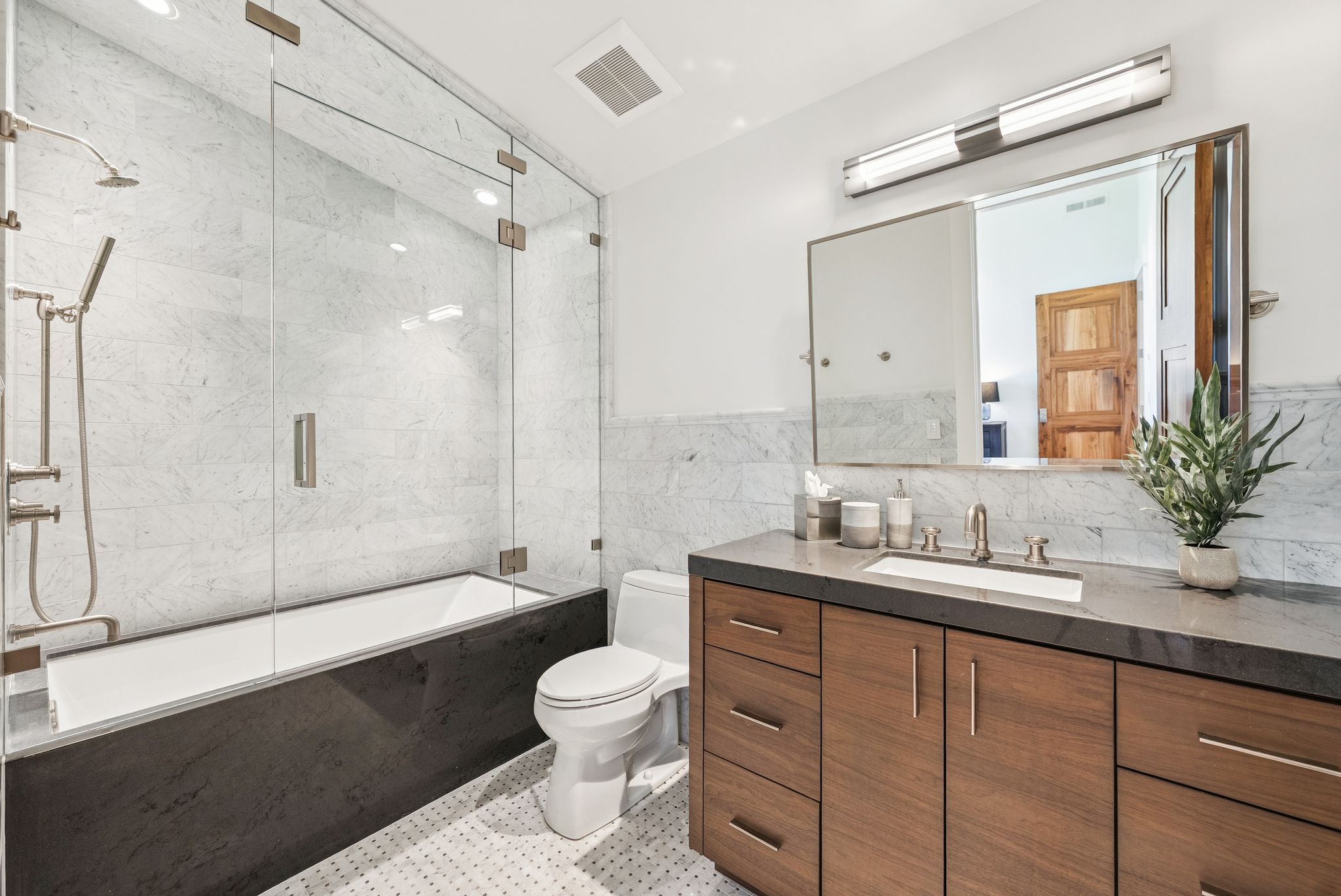 Bathroom with bath / shower combo with glass door, vanity, and tile walls
