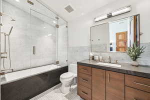 Bathroom with bath / shower combo with glass door, vanity, and tile walls