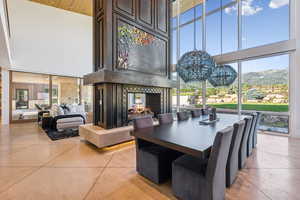 Dining area featuring a high ceiling, a multi sided fireplace, a chandelier, a mountain view, and light tile patterned floors