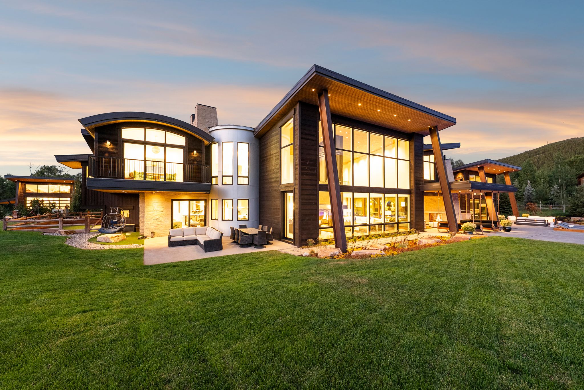 Back of house at dusk with an outdoor living space, a balcony, a lawn, a patio, and a chimney