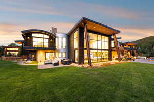 Back of house at dusk with an outdoor living space, a balcony, a lawn, a patio, and a chimney