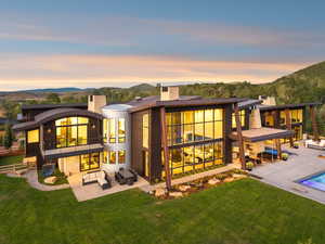 Back of property at dusk with an outdoor hangout area, a balcony, a chimney, a patio, and an outdoor pool