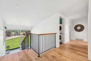 Hall with stacked washer and clothes dryer, wood finished floors, an upstairs landing, and recessed lighting