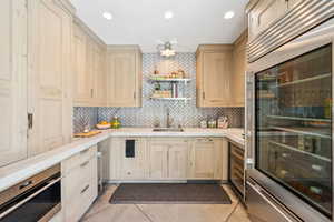 Kitchen featuring wine cooler, backsplash, light brown cabinetry, stainless steel appliances, and open shelves