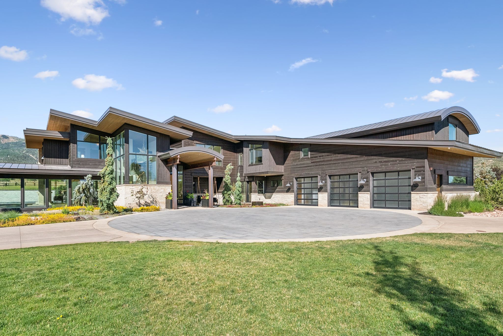 Contemporary home with decorative driveway, an attached garage, a front lawn, a metal roof, and stone siding