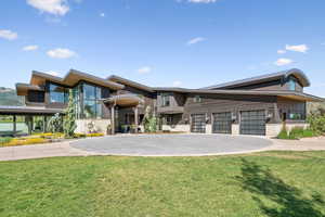 Contemporary home with decorative driveway, an attached garage, a front lawn, a metal roof, and stone siding