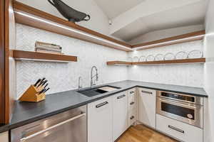 Kitchen featuring open shelves, stainless steel appliances, lofted ceiling, dark countertops, and tasteful backsplash