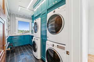 Washroom featuring cabinet space, stacked washing machine and dryer, and attic access