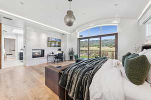 Bedroom featuring access to outside, light wood finished floors, a multi sided fireplace, vaulted ceiling, and recessed lighting